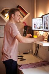 one young man, 20-29 years old, looking to two computer monitors, while working on a computer in his room, at his home. using standing desk.