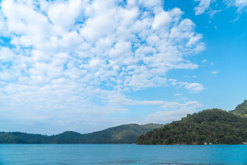 Obraz premium Mountains landscape scene with blue sky and white clouds over green water in sun moon lake in Taipei, Taiwan