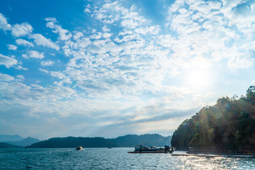  Mountains landscape scene with blue sky, white clouds and sunshine with lens flares over green water in sun moon lake in Taipei, Taiwan
