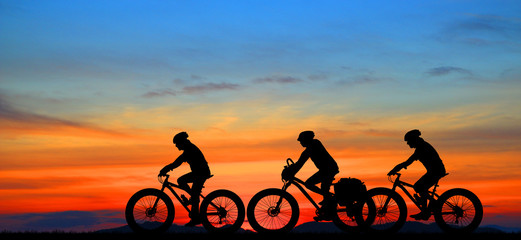 Silhouette group friend  and bike relaxing on blurry sunset background.