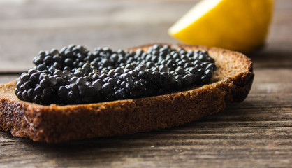 black caviar on rye bread with a lemon and a silver spoon on a background of moss and wood.