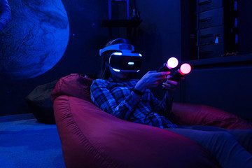Man plays virtual reality using glasses, gamepad and headset.