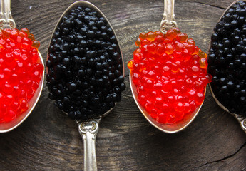 Red and Black caviar beads on silver spoon on wooden background.Top view