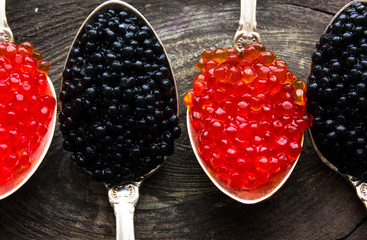 Red and Black caviar beads on silver spoon on wooden background.Top view