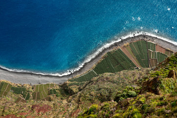 Top view of the coast of the island of Madeira with a coastline and areas with planted plants. Cropped shot, top view, free space for text, horizontal. Nature and agriculture concept.