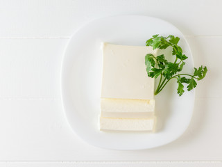 Parsley with a piece of Serbian cheese on a white plate. The view from the top. Dairy product.