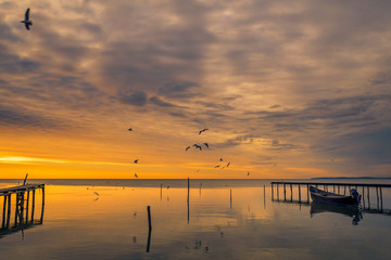 Fototapeta na wymiar Lake scene in the morning at sunrise with birds flying above the lake and a boat near a pontoon