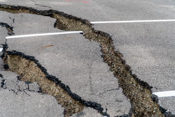 Damaged parking lot collapses with huge cracks by natural disaster. Asphalt parking lot collapse and falling down until found structure from bad construction.