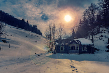Small abandoned house found on the hills with footstepts in the snow guiding to the house shot in the mountains on a winter sunny day