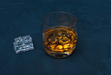 Glass of whiskey with ice cubes on dark blue  background