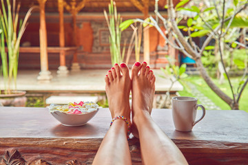 Woman's feet on a desk in a tropical backyard.