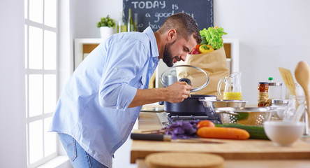 Smiling and confident chef standing in a large kitchen tasting 