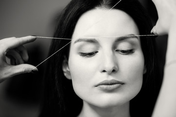 Cosmetologist plucks client eyebrows by thread