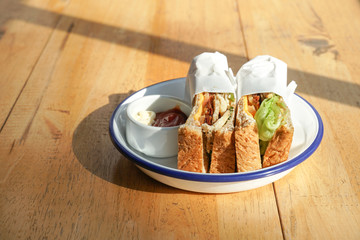 Sandwiches in white plate with ketchup and mayonnaise on a wooden table.