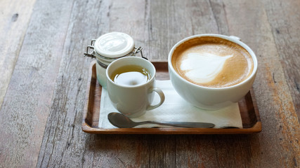 Hot coffee in white ceramic cup and  syrup on wooden table.