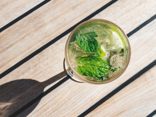 Beautiful glass with refreshing mojito and ice cubes on the background of the plank deck. Top view, close-up. Concept of leisure and travel