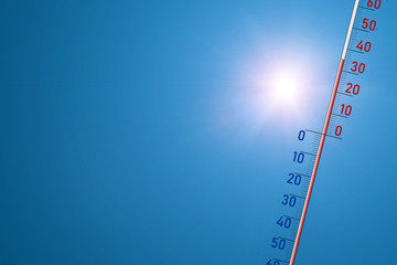 The thermometer on a blue background and in bright sun shows 35 degrees of heat