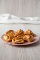 Home-baked cottage cheese biscuits on pink plate over white wooden surface, side view. Close-up.