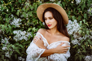 young woman in a straw hat in lilac. Model in white pennuar among flowers
