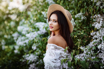 young woman in a straw hat in lilac. Model in white pennuar among flowers