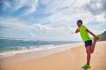 Sportsman stretching on a tropical sandy beach.