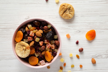 Dried fruits and nut mix in a pink bowl on white wooden background, top view. Overhead, from above, overhead.