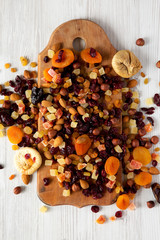 Dried fruits and nut mix on rustic wooden board over white wooden surface, top view. Overhead, from above. Close-up.