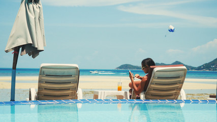 Beautiful young woman using her phone in the beach lounger while take a sunbathing