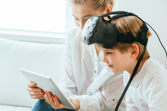 Mother and son with virtual reality headset sitting onsofa using digital tablet. Happy mom and little boy using tablet with touchscreen watching a video. Smiling sister and brother playing on tablet
