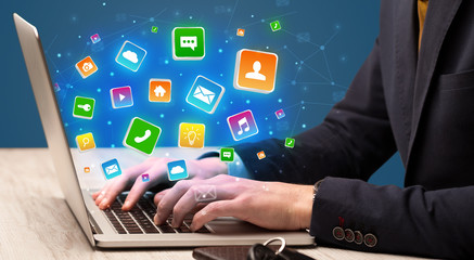 Businessman hand typing on laptop with flying application icons around
