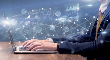 Businessman typing on laptop with linked reports charts grapghs around
