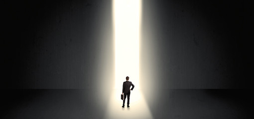 Businessman standing and seeing the light at the end of a big wall
