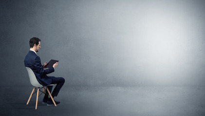 Businessman staying in an empty grey dark room with stuffs on his lap
