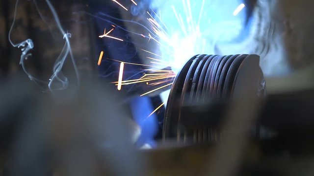 Worker`s hands welding a reel from a thick metallic wire in a dark workshop