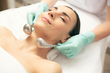 Hands of beautician holding cryo-sticks near the face of woman