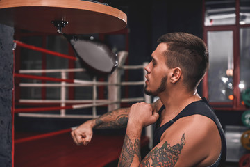 Ready to break his record. Close-up of muscular tattooed boxer in sports clothing hitting punching...