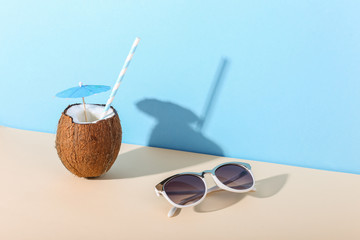 Tropical cocktail in coconut with straw and an umbrella, on paper blue and yellow background. The concept of relaxation, summer mood, copy space