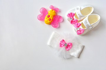 Baby girl accessories background. Pink butterfly teether, booties, headband  on a white table. Top view.