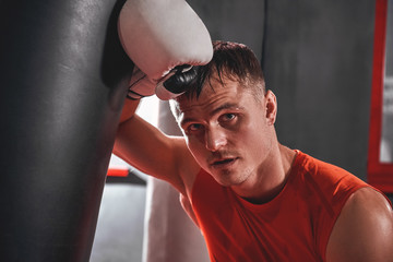 Taking time to rest. Tired young athlete in sports clothing taking break after hard training on heavy punch bag in boxing gym