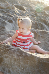 One-year-old baby girl in a red and white dress sitting on the rocky coast, spending time outdoors is important for little ones