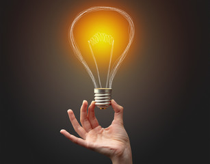 Hand holding light bulb on dark background. New idea concept