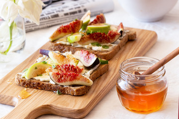 Toasted whole wheat bread with figs, ricotta (cream cheese),mint, honey served on white wooden cutting board. Healthy food concept.
