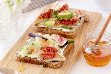 Toasted whole wheat bread with figs, ricotta (cream cheese),mint, honey served on white wooden cutting board. Healthy food concept.