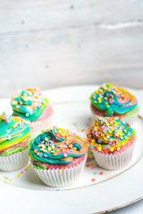 beautiful, bright, very colorful muffins decorated with rainbow cream and candy confetti, on a bright, spring background