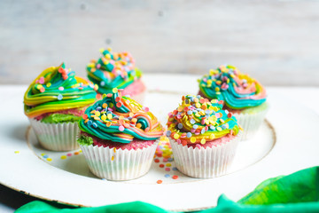 beautiful, bright, very colorful muffins decorated with rainbow cream and candy confetti, on a bright, spring background
