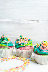 beautiful, bright, very colorful muffins decorated with rainbow cream and candy confetti, on a bright, spring background