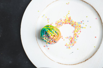 beautiful, bright, very colorful muffins decorated with rainbow cream and candy confetti on a white, wooden plate