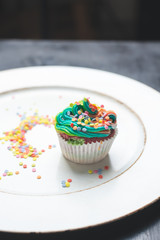 beautiful, bright, very colorful muffins decorated with rainbow cream and candy confetti on a white, wooden plate