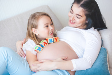 Pregnant woman and her little daughter having fun indoors. Maternity. Young mother waiting for a baby birth with little cute daughter. Family together.