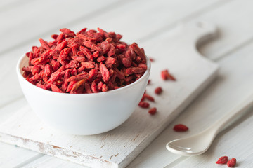 Goji in bowl on white wood table. Top view of fresh goji in scoop and bowl.